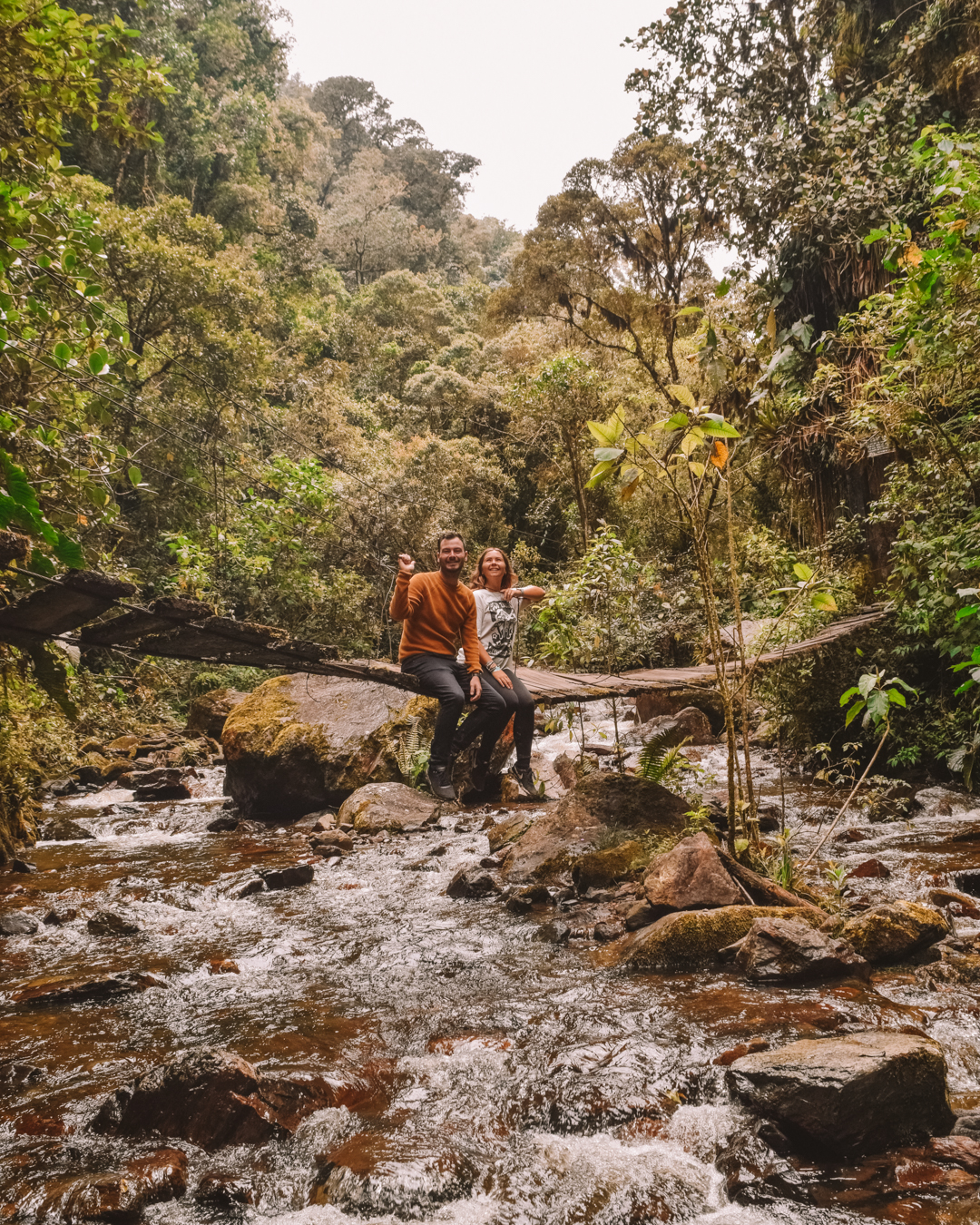 Travel couple sitting on a bridge whilst hiking Cocora Valley (Valle del Cocora) in Salento, Colombia